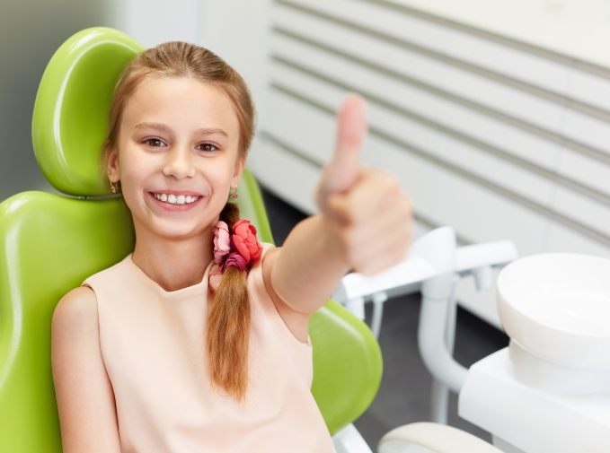 Girl in dental chair giving a thumbs up