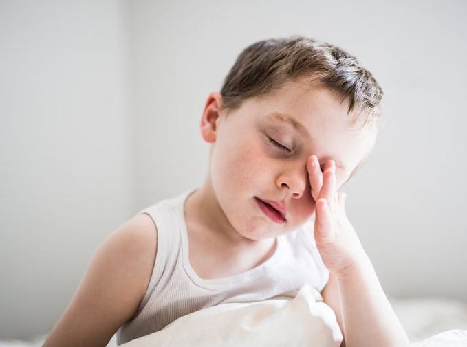 a boy rubbing his eyes after waking up