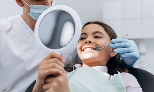 Teen examining their cosmetic dental work in handheld mirror and smiling