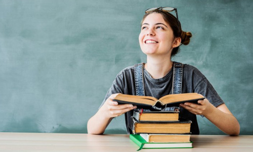 Teen smiling while cracking open a book with a chalkboard in the background