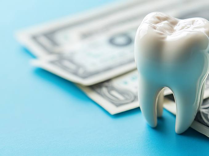 Large model tooth next to dollar bills on blue surface