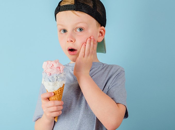 Little boy cringing in pain at tooth sensitivity while holding ice cream