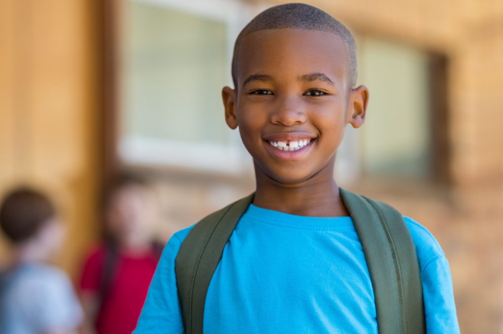 Child with blue shirt and backpack smiling at school