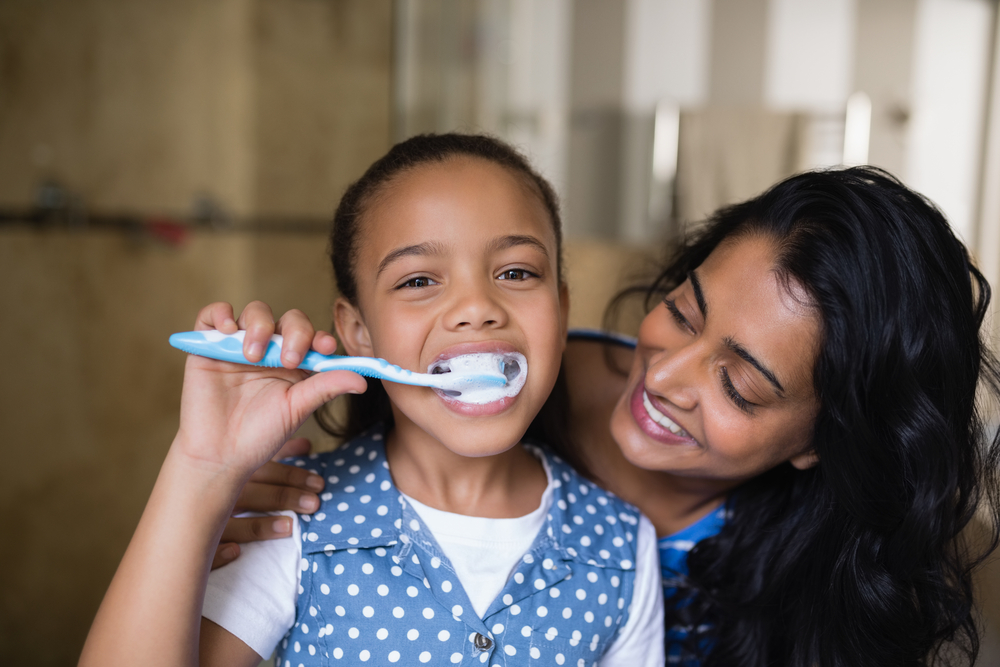 child brushing teeth with parent at home